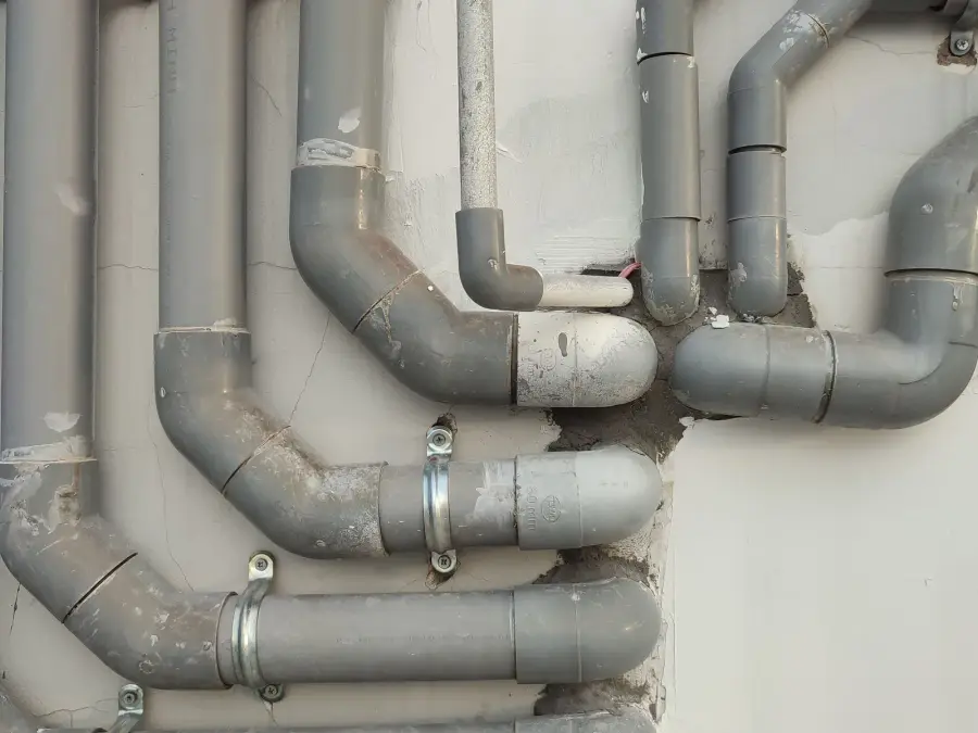 Exterior drain and vent pipework running along the base of a residential wall