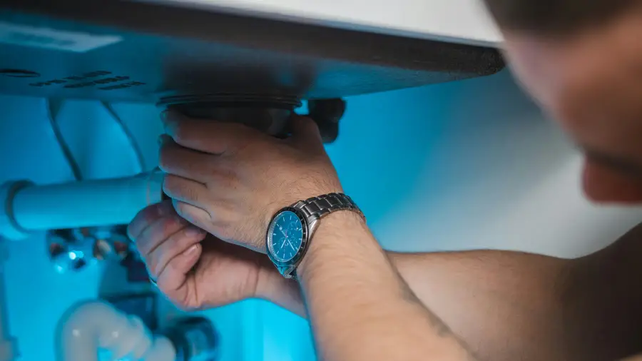 Plumber's hands tightening the P-trap and drain fittings beneath a white bathroom sink