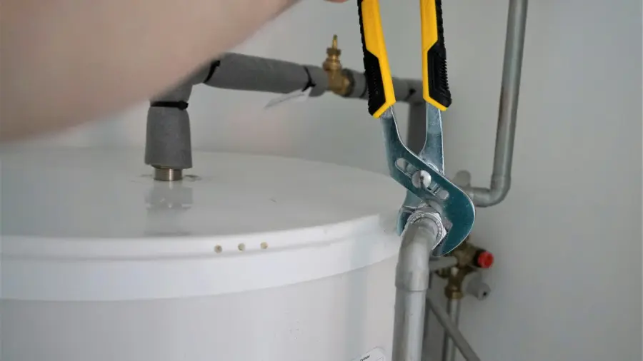 Adjustable wrench on the inlet fitting on top of a white residential tank water heater